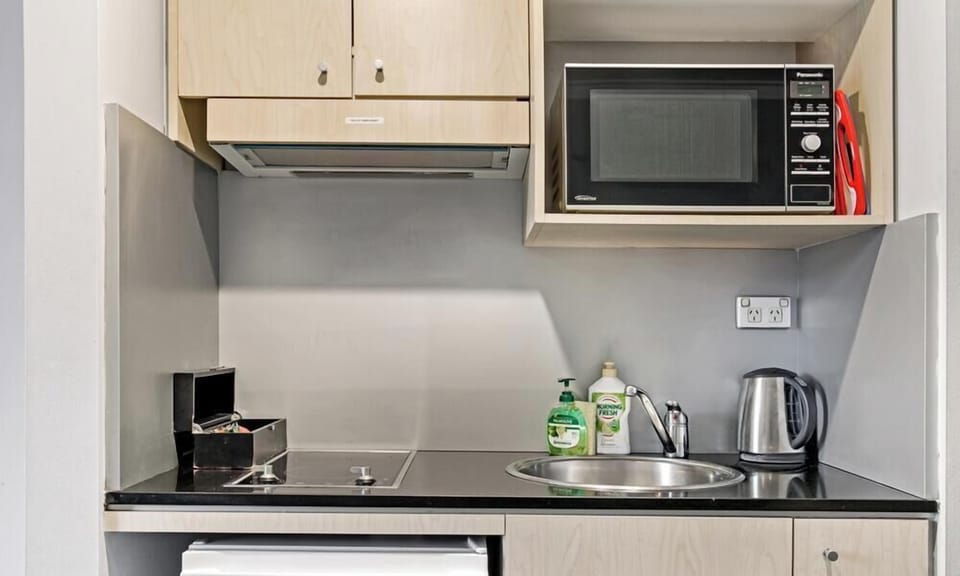 clean kitchen corner equipped with a built-in microwave, an electric stovetop, a small refrigerator, and a stainless steel sink.