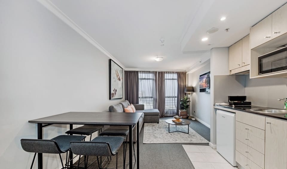 the dining table, compact kitchen countertop, and the living area beyond.