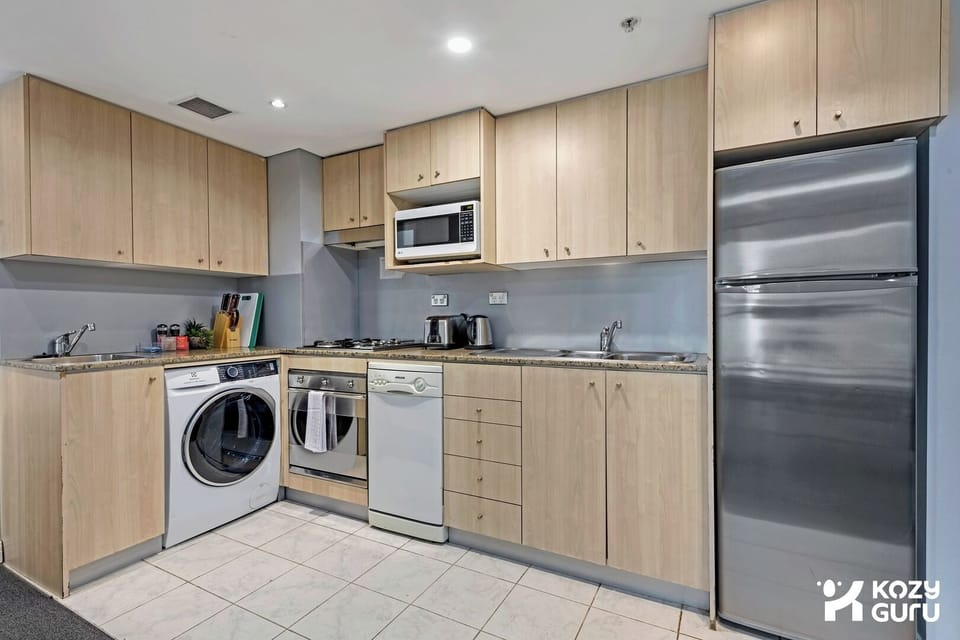 A closer shot of the clean kitchen setup, detailing the wooden cabinets, stainless steel appliances  and refrigerator.