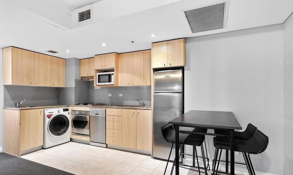 A fully equipped kitchen with wooden cabinetry, stainless steel appliances, a bar-height dining table with stools