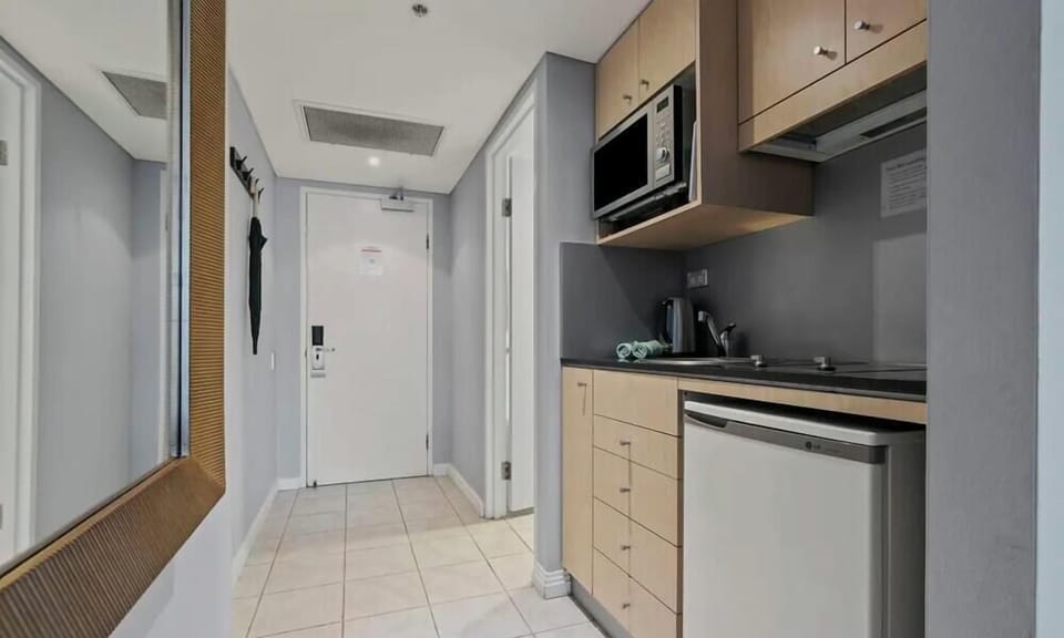 A clean, modern kitchen area with light wood cabinetry, granite-style countertops, integrated stainless steel cooking appliances, and a built-in microwave.