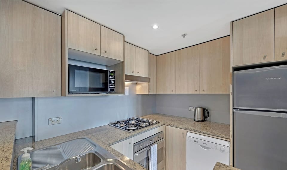 : A tidy kitchen featuring light wood cabinetry, granite-style countertops