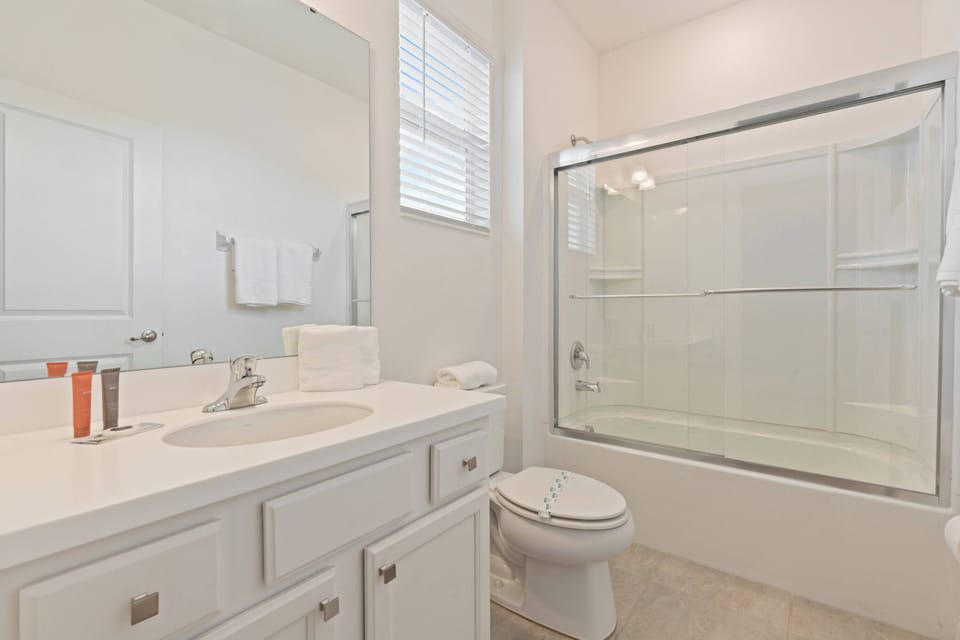 This bright bathroom features a spacious vanity with sleek white cabinetry and a large mirror that enhances the airy feel. The glass shower adds a modern touch, and the neutral tones create a calming ambiance for your relaxation.