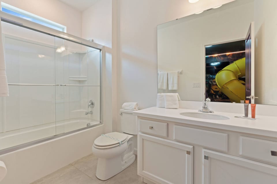 This bright bathroom features sleek white cabinetry and a spacious mirror that enhances the natural light. The glass shower enclosure adds a modern touch, creating a refreshing ambiance for your daily routines.