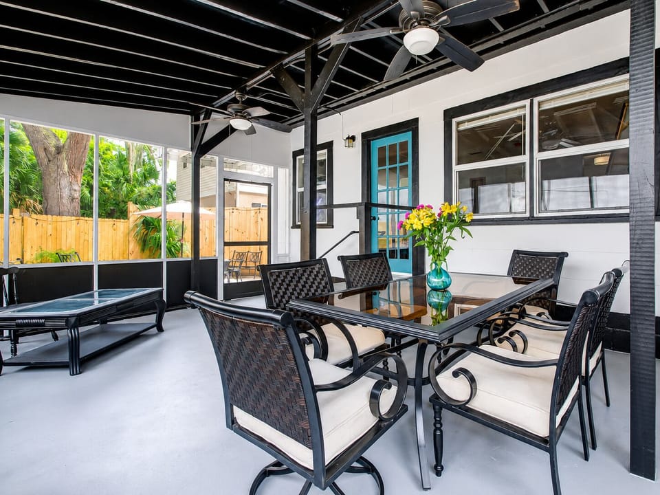 Screened covered patio with dining area, ceiling fans, and tropical privacy