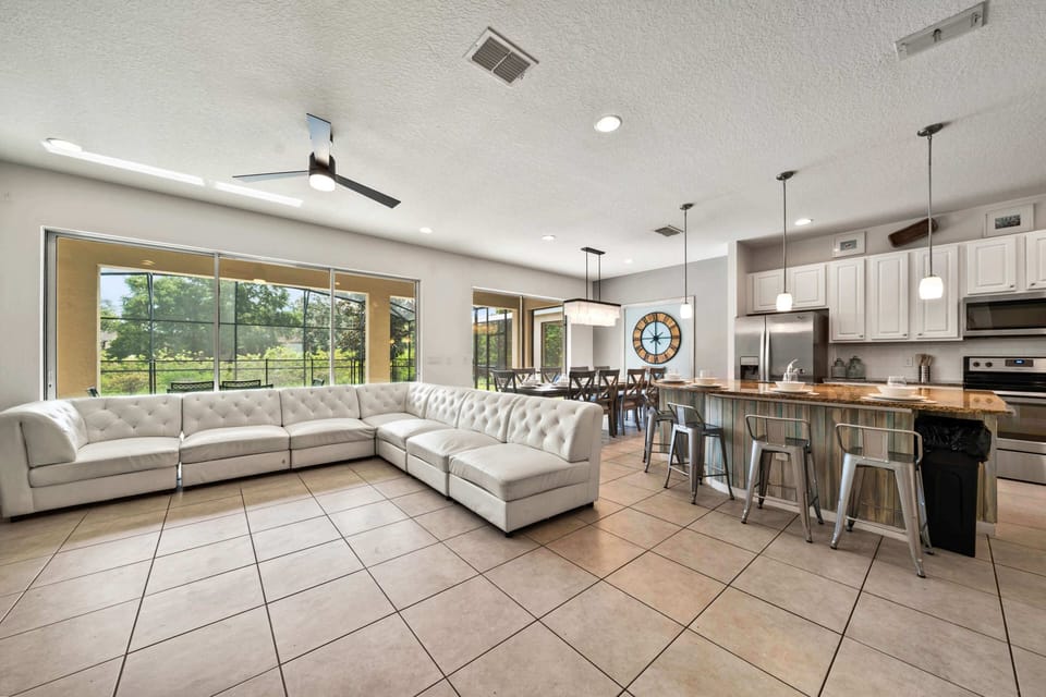 - Open-concept living room with oversized sectional and modern kitchen  
- Dining space and bar seating perfect for large family gatherings  
- Natural light and pool views make this vacation rental feel inviting