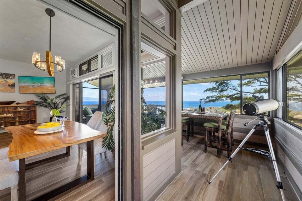Lanai entry with outdoor seating, ceiling fan, and shaded balcony overlooking lush resort grounds and the Pacific Ocean.