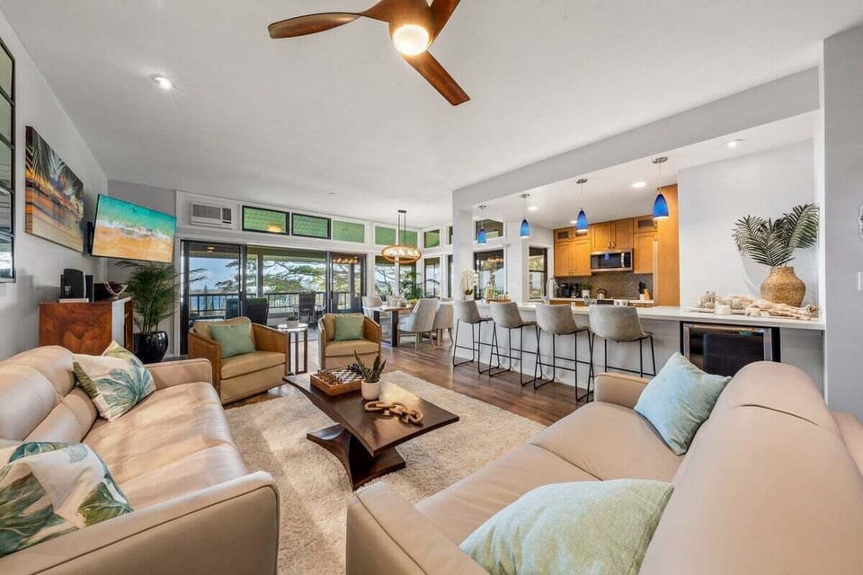 Bright open‑concept living room with new sleeper sofa, smart TV, window AC, and direct access to a spacious oceanview lanai.