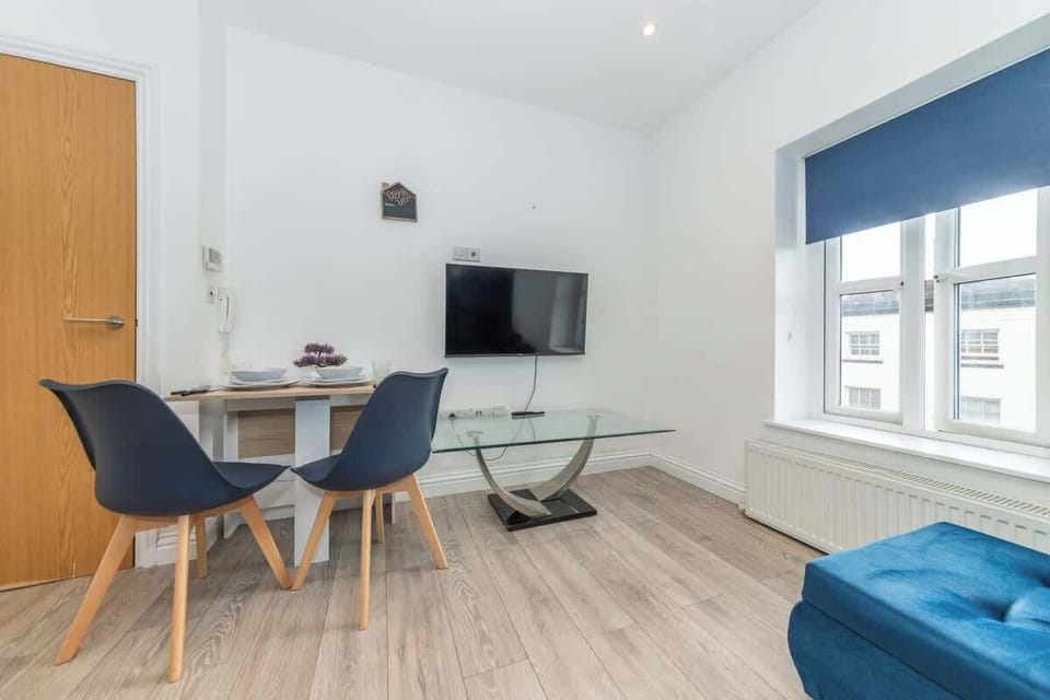 The dining area features a wooden table set for a meal, accompanied by stylish blue chairs and a television on the wall too enjoy movies or watch tv shows after long days to relax.