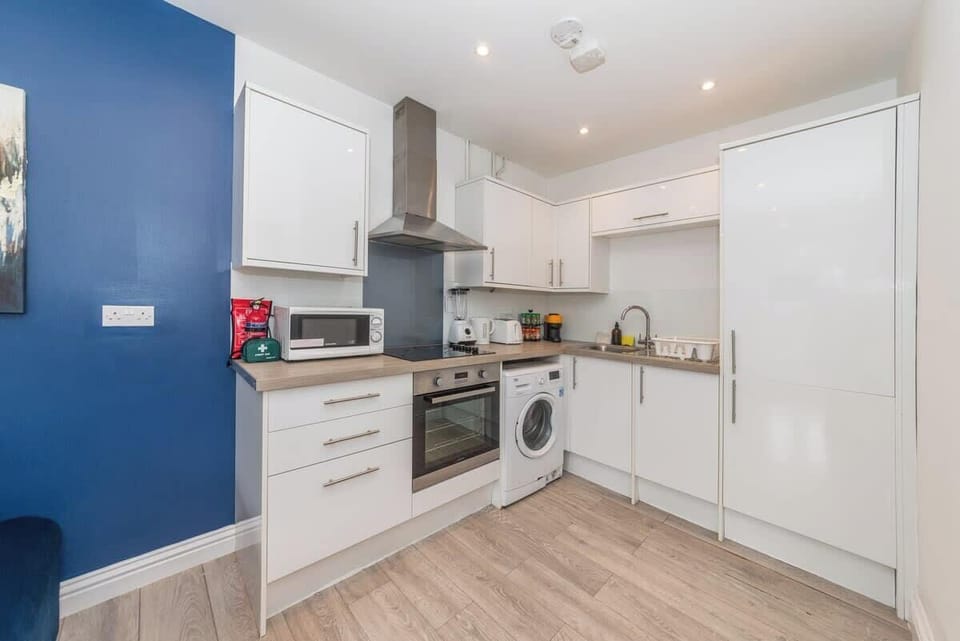The kitchen features modern white cabinetry, stainless steel appliances, and a sleek countertop complemented by a blue accent wall.
