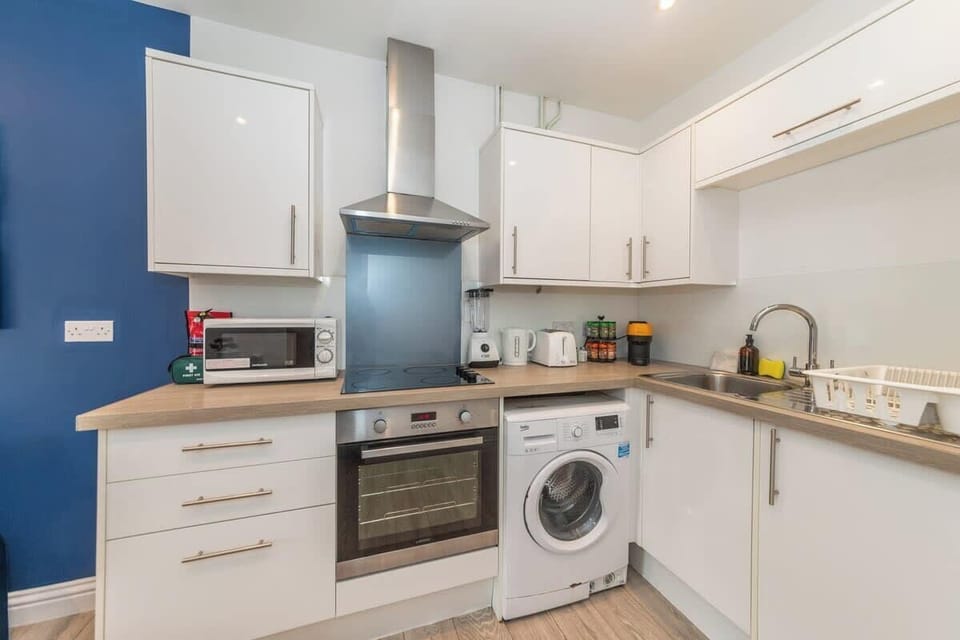 The kitchen features modern white cabinetry, stainless steel appliances, and a sleek countertop complemented by a blue accent wall.