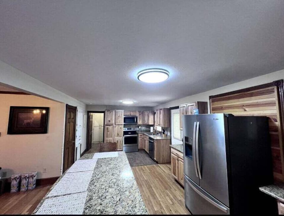 Open-concept hallway with kitchen access, stainless refrigerator, and wood flooring inside this Bryson City Smoky Mountain cabin rental.