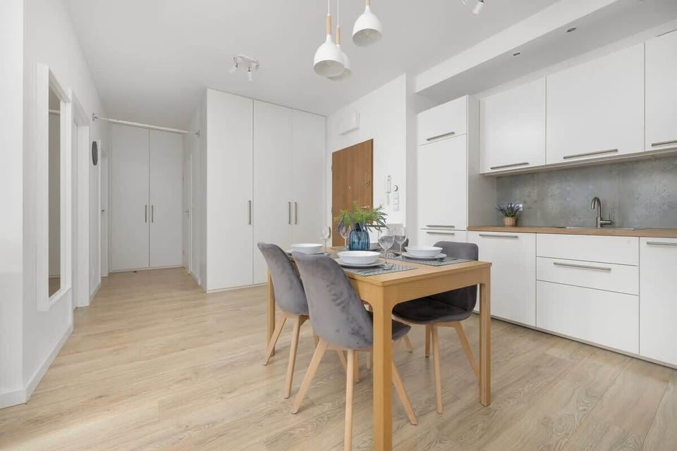 Kitchen with white cabinetry, a dining area with gray chairs, and wooden flooring.