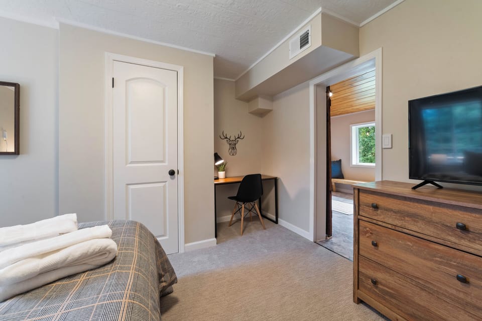 This bedroom features a queen bed, black out curtains, working area with desk, and TV