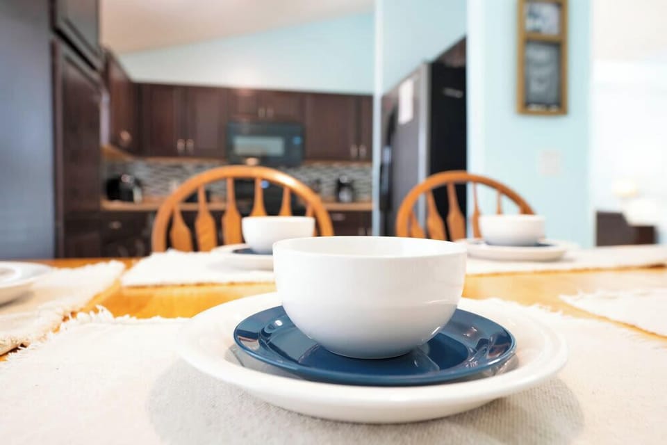 Dining table set with white bowls and blue plates in a kitchen with dark wood cabinets.