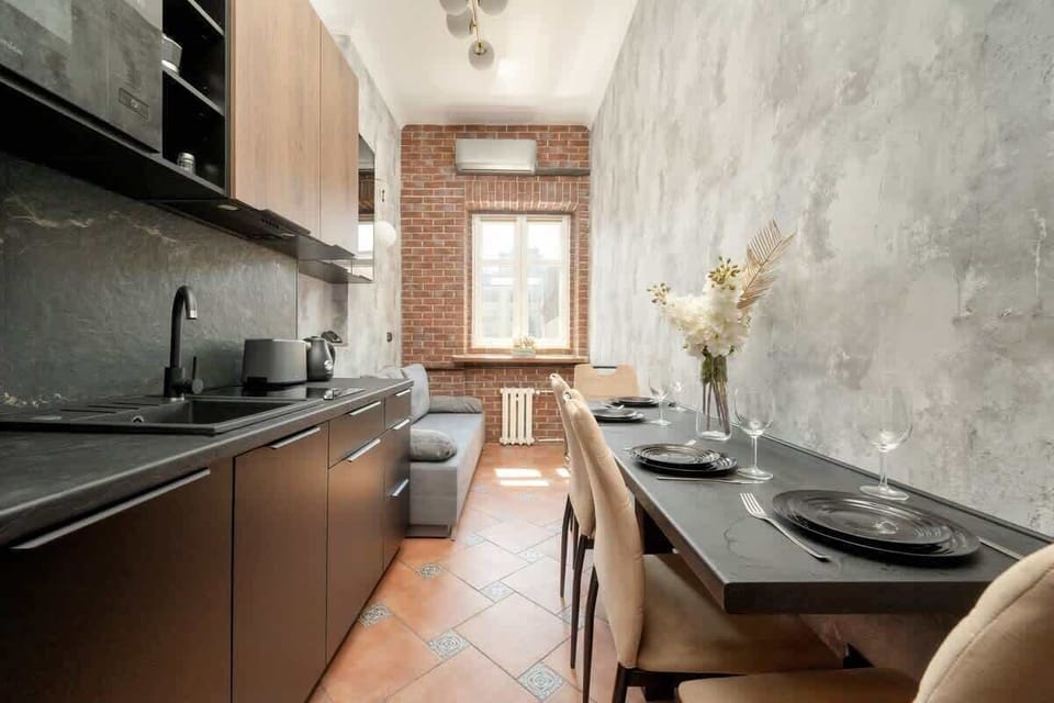 The modern kitchen pairs dark cabinetry with a warm brick-framed window, giving the space both functionality and charm.
