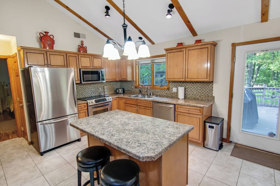 Fully equipped kitchen with stainless steel appliances, island, and deck access.