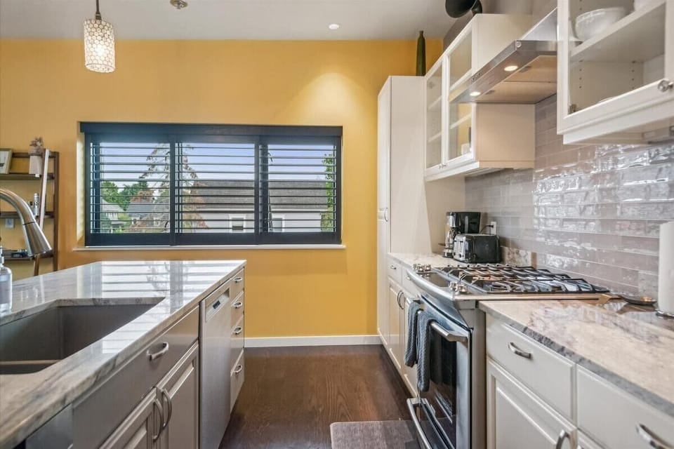 Bright, airy, sunlit kitchen with large windows and light-colored surfaces.
