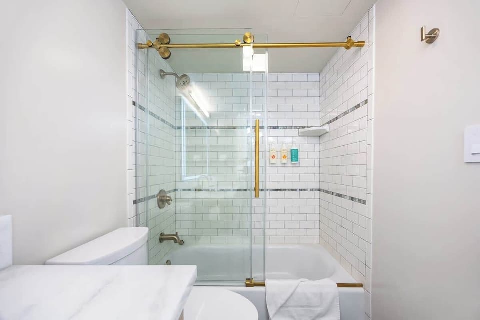 Enjoy a refreshing shower or relaxing bath in this beautifully tiled tub/shower combo, featuring sleek glass doors and stylish gold fixtures!