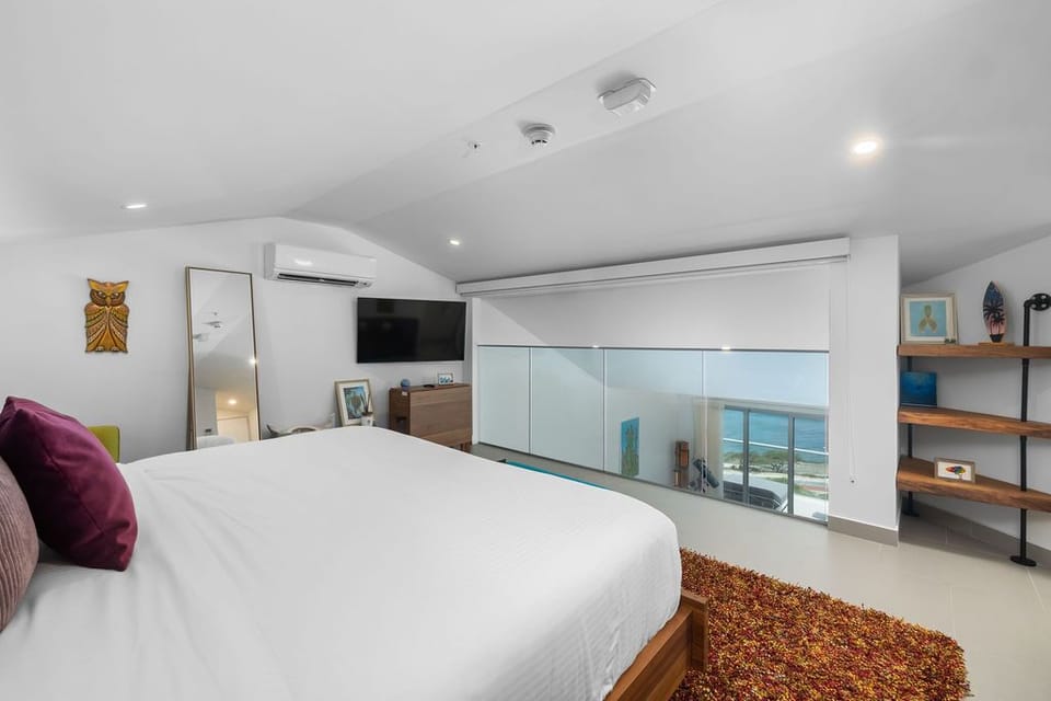 A modern loft bedroom with sea views awaits you, complete with cool air conditioning, wall-mounted TV, and thoughtful shelving for your treasures.