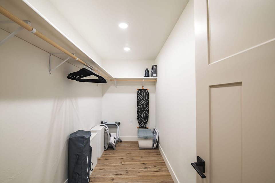 Walk-in closet with hangers, ironing board, pack and play, and high chair.