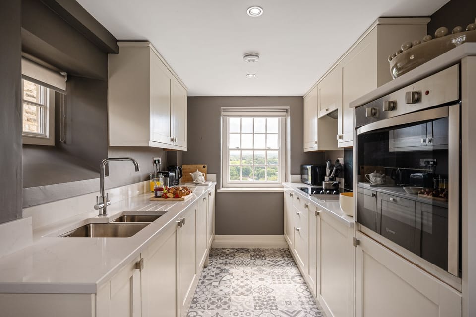 Maison Cottage galley kitchen with modern appliances, white cabinetry and countryside views through the window