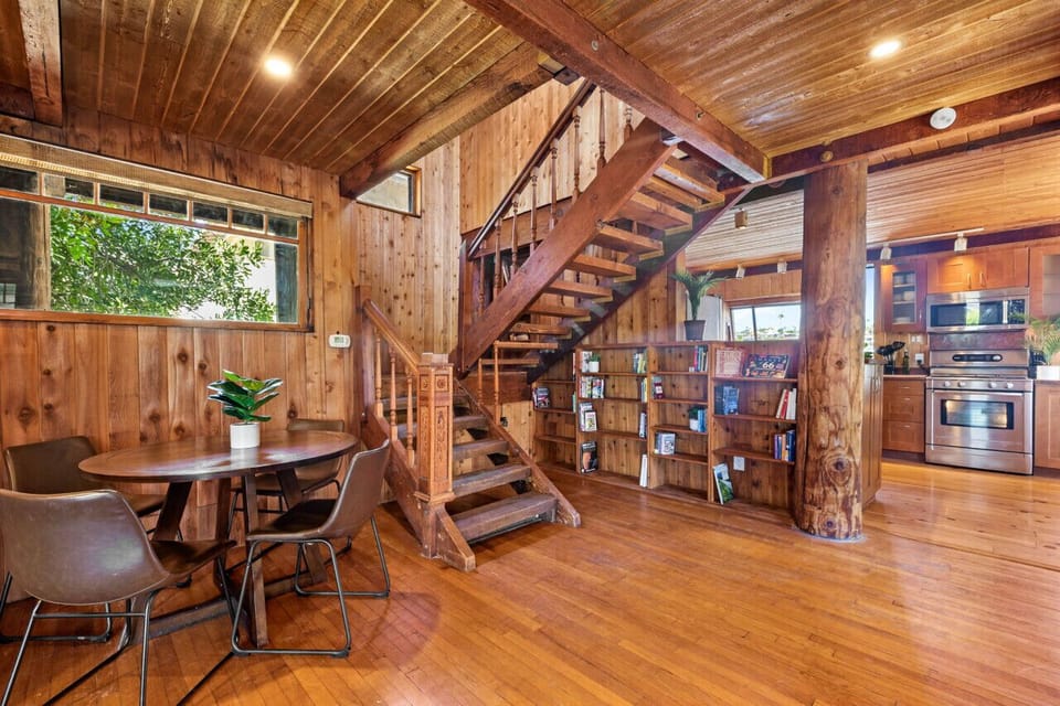 Enjoy cozy meals at the round dining table while admiring the rustic wooden staircase and built-in bookshelf. The kitchen appliances offer modern conveniences in a charming setting.