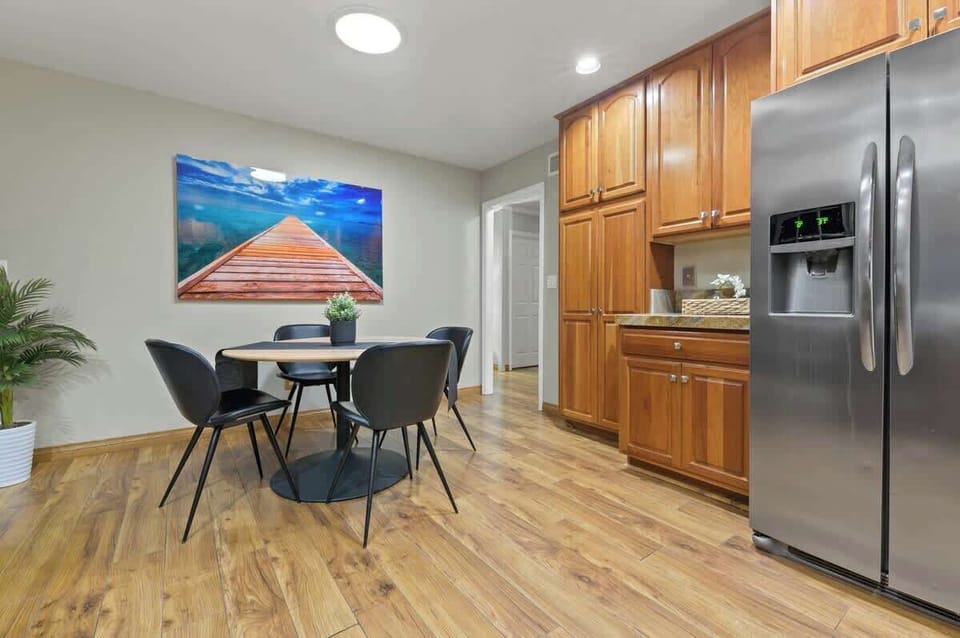 The Scandinavian-inspired dining set, featuring a sleek black and wood theme, complements the rich wood cabinetry. A 2-door premium refrigerator adds both style and functionality, while the well-lit room creates a warm and inviting atmosphere.