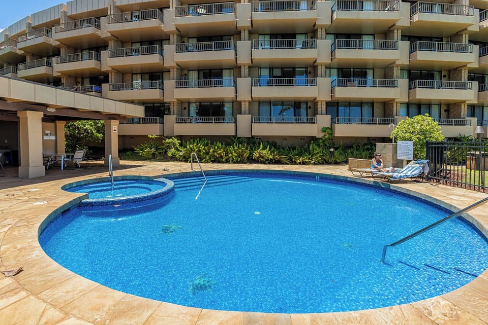 A multi-level property featuring tiered balconies, lush tropical landscaping, and an inviting curved pool with attached spa, providing a resort-style atmosphere for your stay.