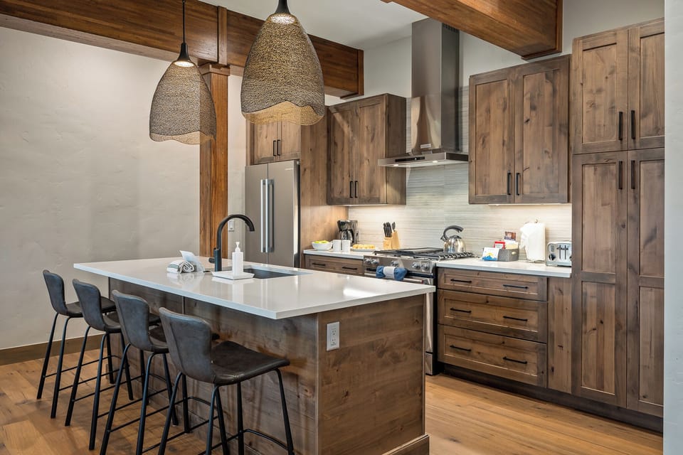 Cook, serve, and gather in this show stopping kitchen with wood cabinetry and sleek island - Two woven pendant lights hang above the counter for ambiance and function - Plenty of space for prep!