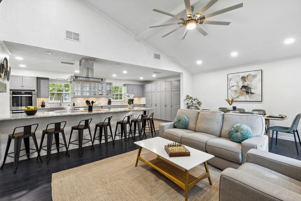 Open-concept living room: gray sofa, wood coffee table, fireplace & staircase