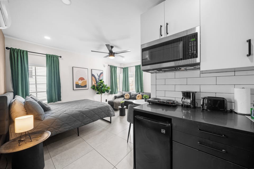 This studio features a kitchenette with a microwave, 2-burner stove, mini-fridge, toaster, and coffee maker, making meal prep easy. The cozy queen-size bed and stylish living area provide a relaxing environment, filled with natural light.
