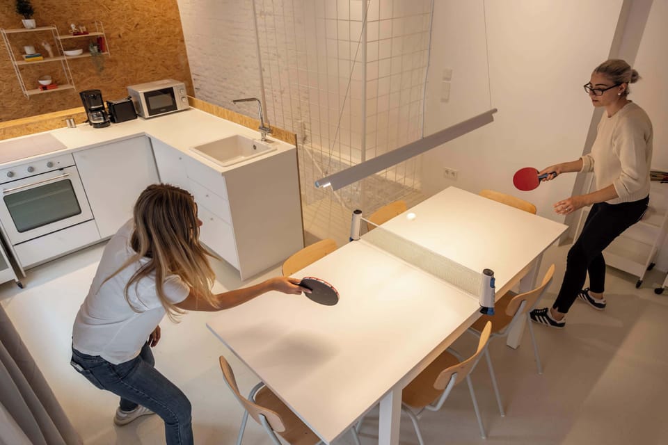A top-angle view of the dining table transformed into a ping-pong station — blending fun with clean Nordic design.