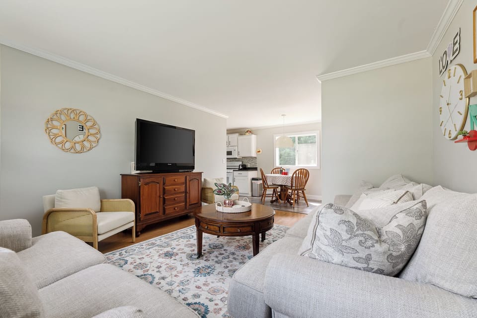 This view of the living room with a large flat-screen TV on a wooden cabinet and a round coffee table in the center.