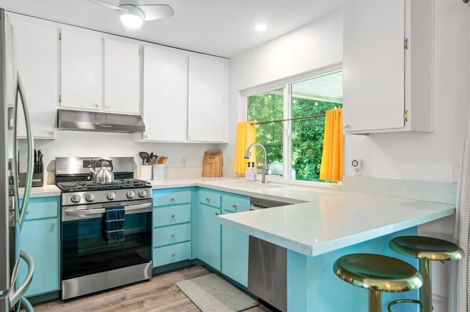 Retro Charm Meets Modern Convenience! 🍽️💫 This fully stocked kitchen blends vintage-inspired turquoise cabinetry with sleek stainless steel appliances for a stylish yet functional space. Natural light pours in through a garden-facing window, creating a br
