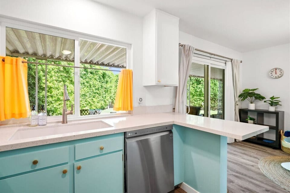 Retro Charm Meets Modern Convenience! 🌟🍴 This stylish kitchen blends vintage-inspired turquoise cabinetry with sleek stainless steel appliances, creating a space that’s both fun and functional. Large windows bring in natural light and a view of lush green