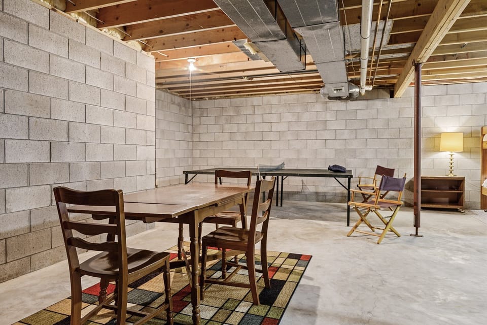 Unfinished basement hangout w/ ping-pong table, wood table & rustic stone walls.