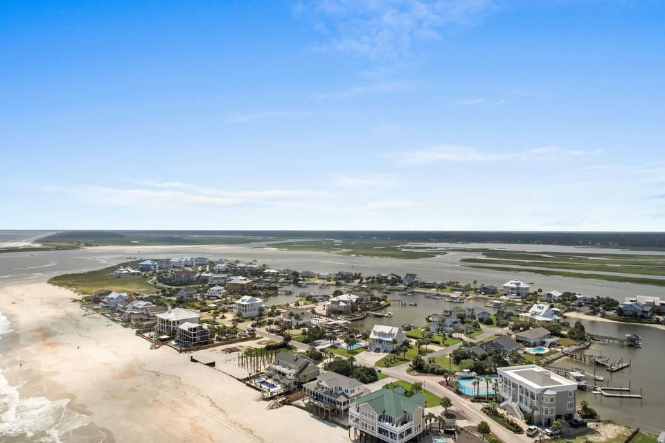 Aerial view of a charming coastal community nestled between pristine beaches and protected marshlands, featuring waterfront homes and docks.