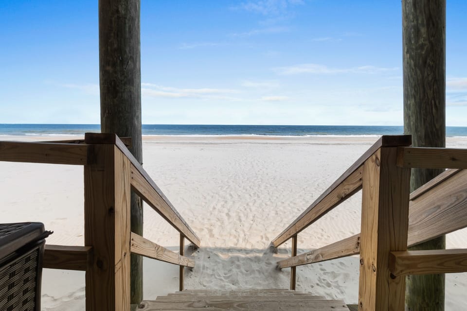 Wooden boardwalk leads directly to pristine white sand beach with crystal blue waters stretching to the horizon.