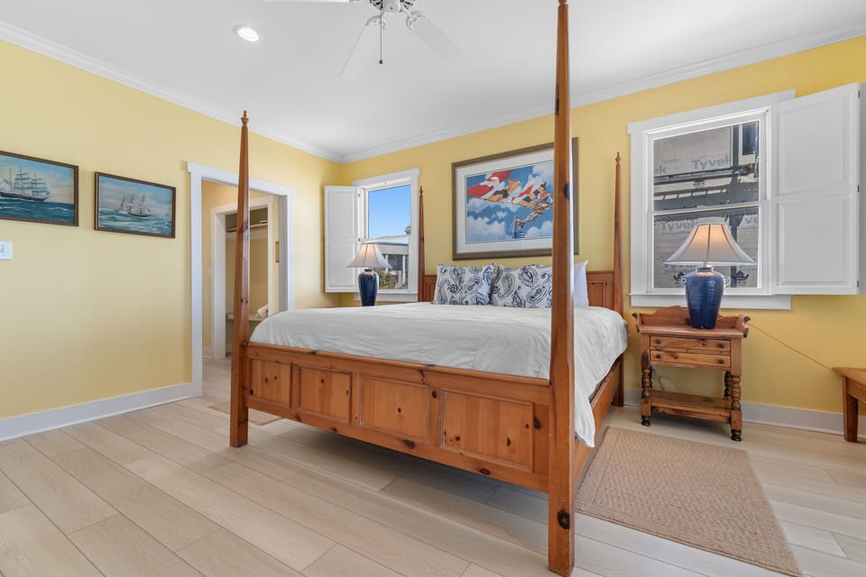 Your sunny bedroom features a handcrafted four-poster bed with crisp linens, nautical artwork, and warm yellow walls that invite restful nights.
