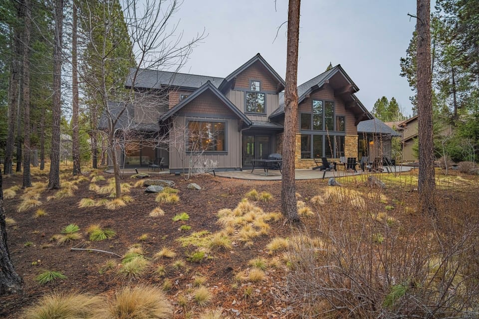 Modern mountain retreat nestled among towering pines with natural landscaping and expansive windows.