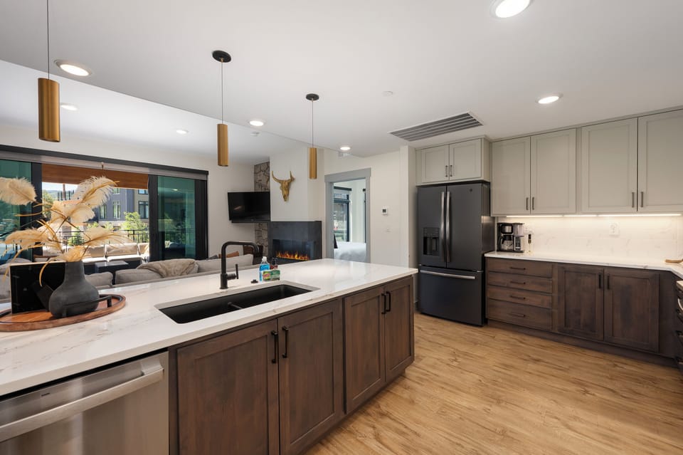 - Cook and connect in this sleek, open kitchen featuring quartz counters and a spacious island - Black fridge, modern lighting, and neutral cabinetry offer a clean, contemporary look - Perfect for prepping meals while staying part of the conversation
