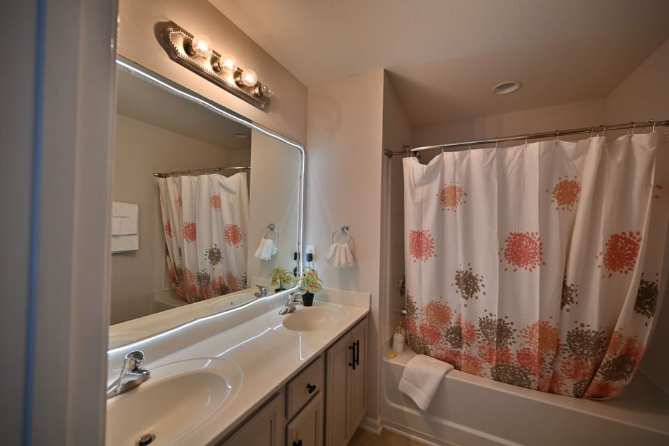 Master bath with double vanity, bright lighting, and bold shower curtain