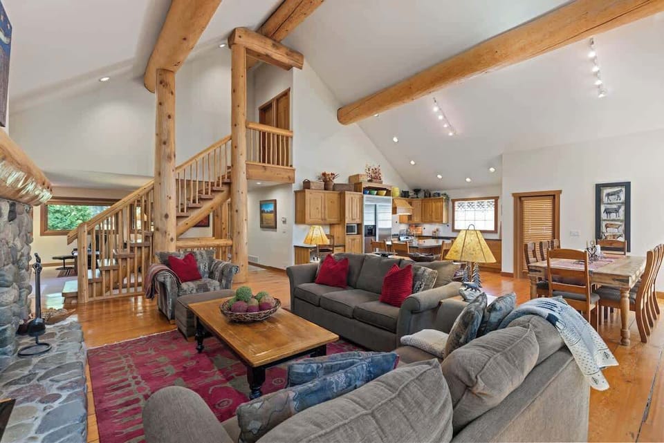 - Spacious open-concept living with rustic log beams and bright windows filling the room with mountain light  
- Plush sofas gathered by the stone fireplace for warm cozy evenings  
- Perfect for gatherings family movie nights or après-ski relaxation