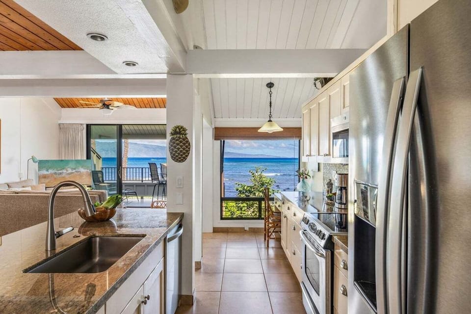 Kitchen features modern and stainless steel appliances, white cabinetry, granite countertop and large window overlooking the Pacific