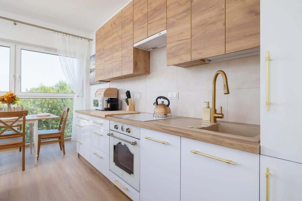 Sleek and modern kitchen with white cabinetry, elegant gold fixtures, and light wood accents that offer both functionality and aesthetic appeal.
