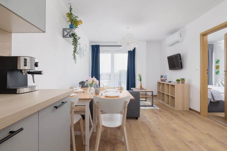 A bright, open kitchen with white cabinets, wooden flooring, and a dining table decorated with plants.