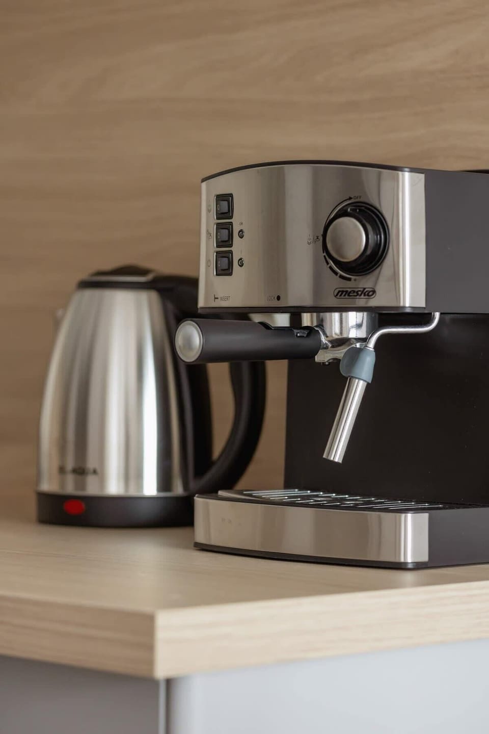 A close-up of a coffee machine and kettle on a wooden countertop.