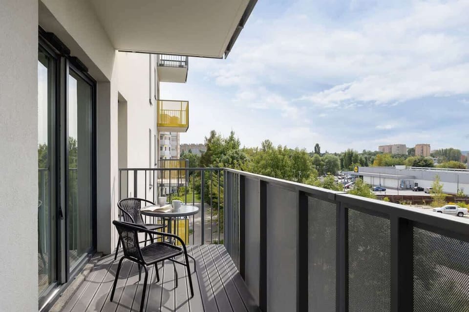 Outdoor balcony with two chairs and a small table, overlooking greenery and a water body.