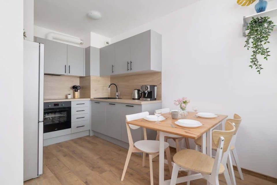 A bright kitchen with white cabinets, built-in appliances, and a small wooden dining table set for two.